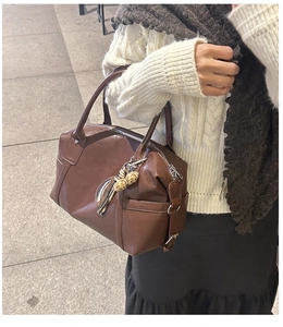 Detail of dark brown Boston bag with peanut pendant and leather texture on a white sweater
