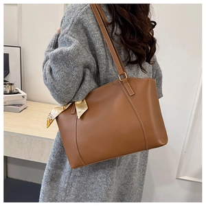 Detail of a brown leather tote bag with white stitching and floral silk scarf detail