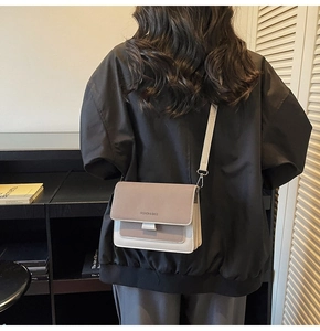 Detail of two-tone beige and taupe crossbody bag with adjustable wide strap on model