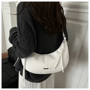 Détail du sac croissant blanc montrant la texture cuir mat, les pompons et la barre en métal