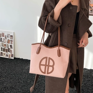 Pink woven tote bag with brown leather trim and circular logo for casual daily commuting