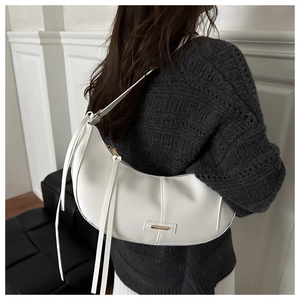 Close-up of white crescent shoulder bag with fringe details and gold-tone metal hardware