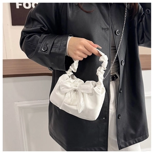 Detailed view of white ruched handbag with bow and metal chain on model