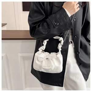 Détail d'un sac plissé blanc avec un grand nœud et une bandoulière en chaîne argentée