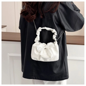 Detailed view of white pleated handbag with oversized bow and metal chain strap