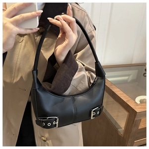 Detail einer schwarzen Halbmond-Tasche mit silbernen Ösen und verzierten Lederriemen