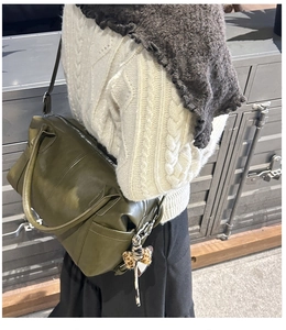 Olive green tote bag with leopard bow charm shown in a stylish crossbody carry style