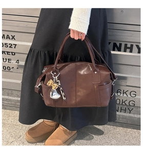 Detailed view of a brown faux leather boston handbag with metallic heart charm and leopard accent