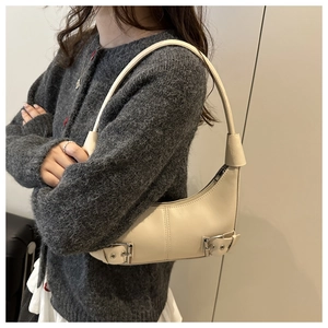 Detail der beigen Halbmond-Tasche mit Metallschnallen vor grauem Strickpullover-Hintergrund