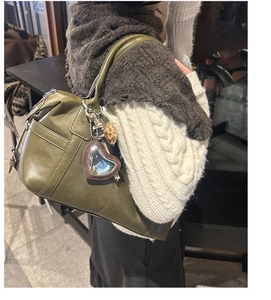 Detail of olive green leather tote bag featuring a heart charm and plush accessory