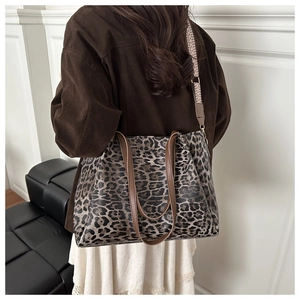 Macro detail of large leopard print tote bag featuring brown leather handles and wide strap