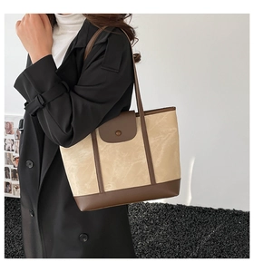 Detail of a large capacity tote bag featuring beige canvas and dark brown leather accents