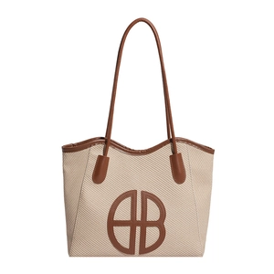 Large beige woven tote bag with brown leather trim and circular HB logo detail