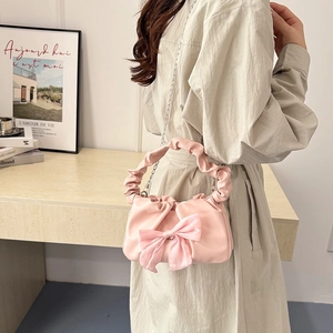 Pink satin handbag with ribbon bow and metal chain strap shown in a lifestyle setting