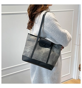 Detailed side view of a grey tote bag with black leather handles held by a model