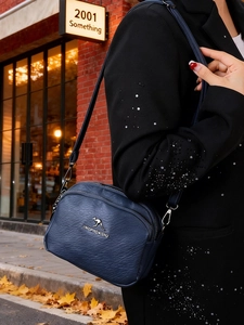Détail du sac bandoulière bleu marine texturé avec logo kangourou en métal doré