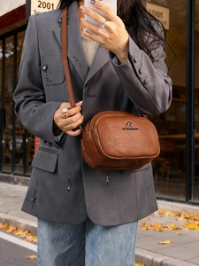 Détail du sac bandoulière en cuir grainé marron avec logo kangourou doré et doubles zips