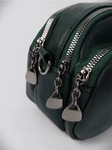 Détail du sac en cuir vert foncé montrant les trois fermetures éclair et l'anneau en D