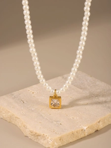 Dettaglio della collana di perle con ciondolo quadrato dorato su base di pietra beige