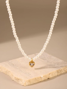 Dettaglio di una collana di perle elegante con ciondolo a cuore dorato e zircone lucente
