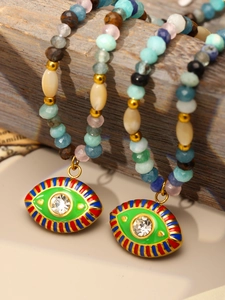 Detail shot of two beaded Evil Eye necklaces hanging on vintage wood with green enamel pendants