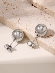 Detailed view of high-polished silver steel ball earrings on a stone platform