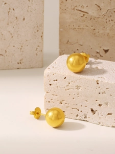 Macro view of polished 18K gold-plated steel ball earrings on travertine stone decor
