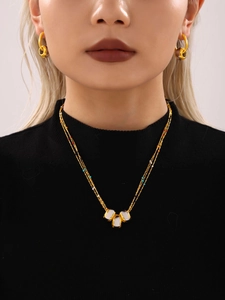 Detailed view of triple-layer gold necklace with white pendants on black turtleneck