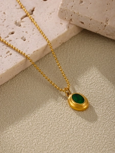 Detail van 18K vergulde kralenketting met smaragdgroene hanger op een stenen achtergrond