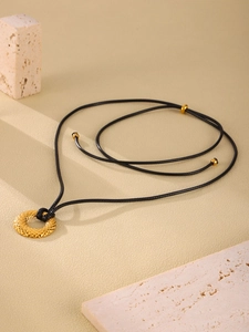 Primer plano del colgante dorado texturizado con cordón negro sobre base de piedra