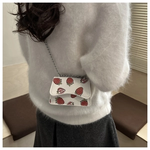 Close-up of a white strawberry print crossbody bag with silver chain on a white sweater