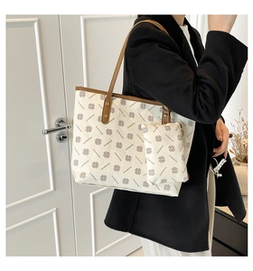 On-shoulder view of large beige tote bag with floral patterns and brown straps