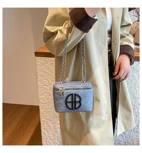 Détail du sac à bandoulière bleu clair texturé avec bandoulière chaîne et logo rond