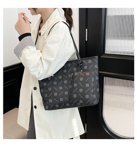 Detail of black tote bag with clover print and matching pouch shown on a model