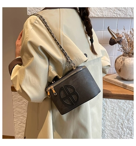 Detail of grey leather crossbody bag with gold BB logo worn with a khaki trench coat