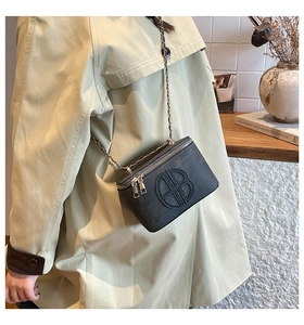 Detail of a black geometric textured crossbody bag with gold leather chain and sleek logo