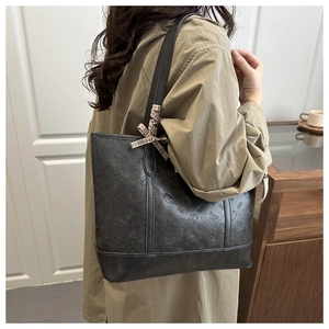Detail of black tote bag with Bread Cat embossing and a plaid bow on a khaki coat