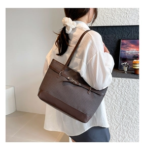 Détail d'un sac cabas tissé marron foncé avec lanières en cuir et boucles métalliques