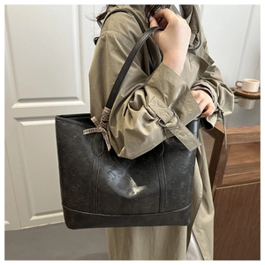 Detail of dark grey embossed tote bag featuring cat patterns and a plaid bow accessory