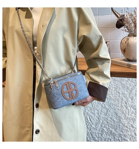 Detail of light blue tweed box bag with brown leather BB logo worn by a model in a trench coat