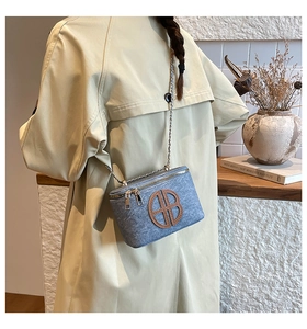 Détail du sac carré en feutre bleu clair avec logo en cuir et chaîne dorée sur mannequin