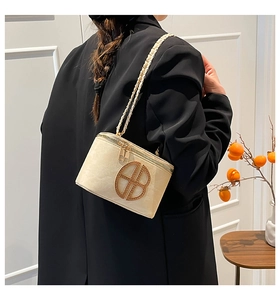 Gros plan d'un sac bandoulière beige en daim avec logo doré et chaîne métallique