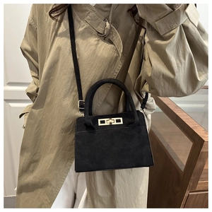 Detail of a black matte crossbody bag featuring a classic gold twist lock on a khaki trench coat