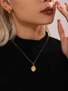 Close-up of a gold religious icon necklace and sparkling diamond-set hoop earrings