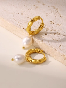 Close-up of 18K gold plated twist hoops with natural freshwater pearl pendants on travertine