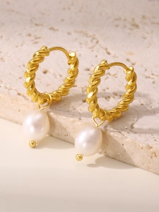 Macro shot of twist gold earrings with natural white teardrop pearls on stone