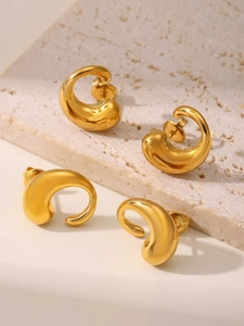 Detailed view of polished 18K gold-plated teardrop C-shape earrings on travertine stone