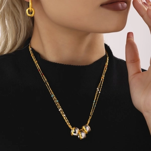 Multi-layer gold-toned bead necklace with two-tone cylindrical pendants on a model