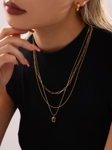 Close-up of layered gold necklaces with black rectangular pendant and beaded chains
