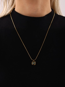 Close-up of a gold square malachite pendant necklace worn on a black knit sweater